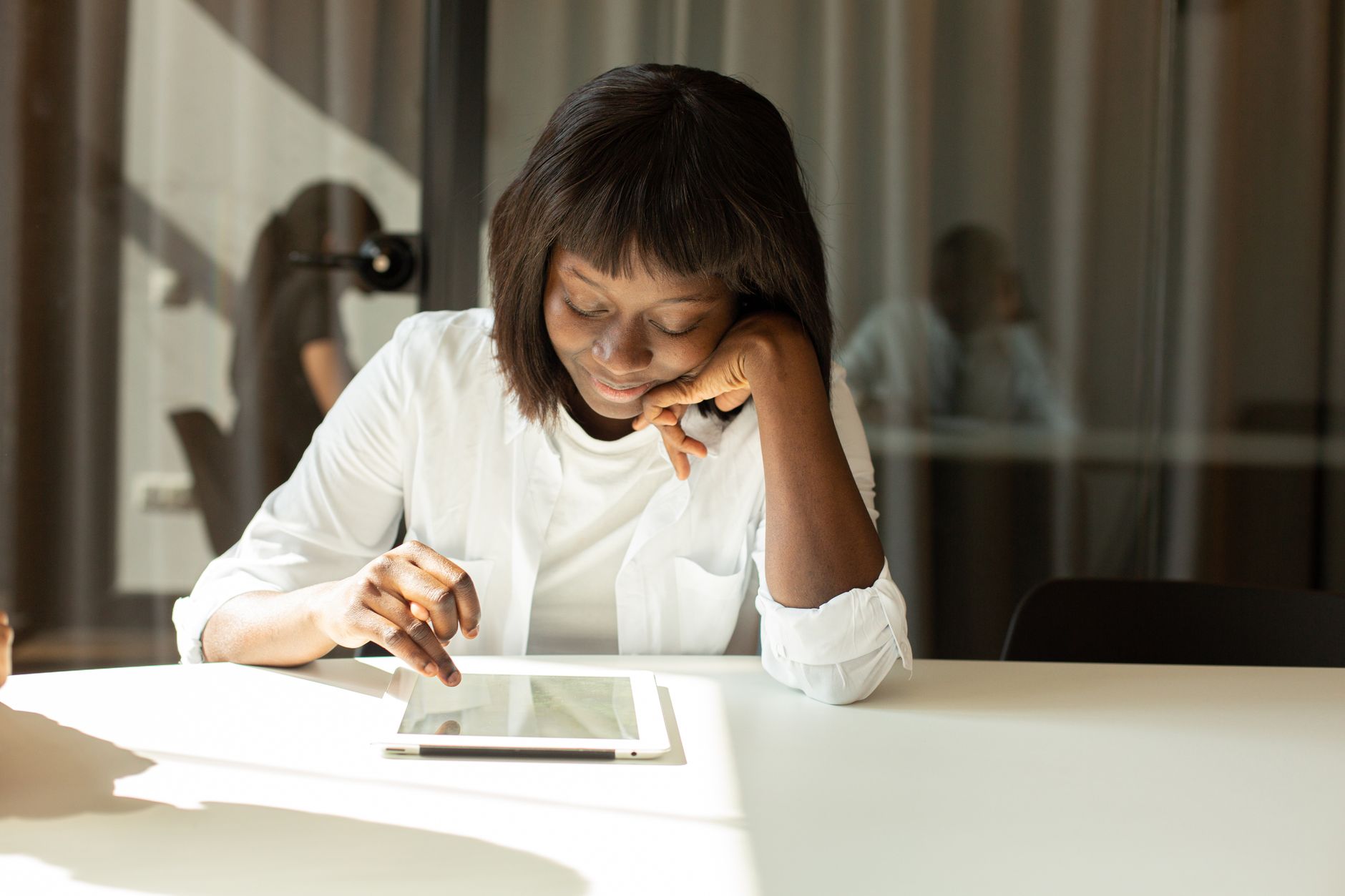 A woman working at a tablet in a sunlit office.