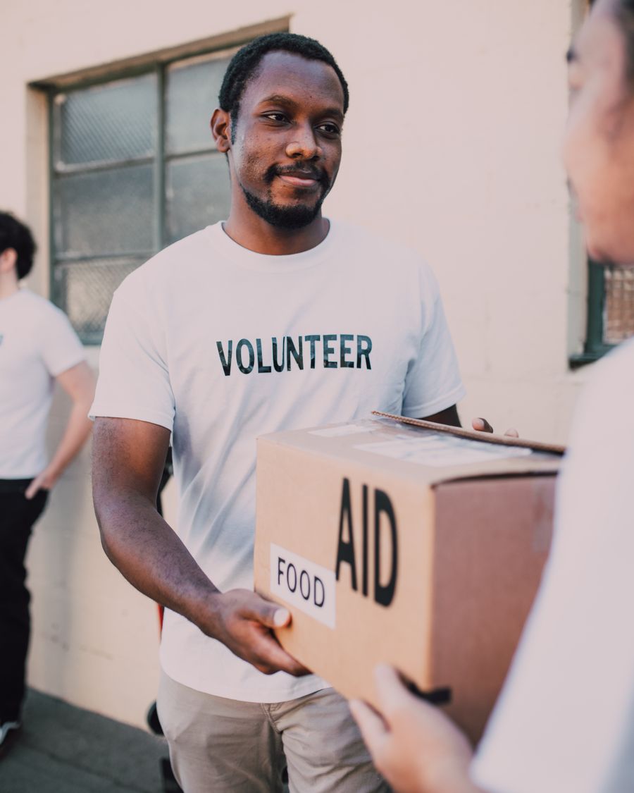 A volunteer in a white shirt holding a cardboard box marked aid and food.